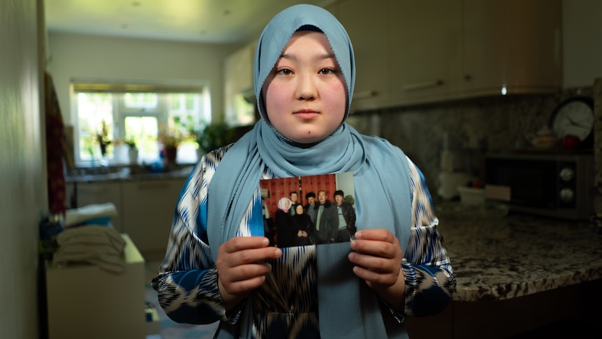 A woman in a headscarf poses with a photo of family members in her hands.
