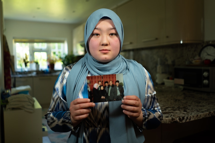 A woman in a headscarf poses with a photo of family members in her hands.