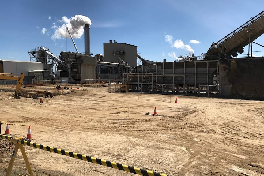 Construction site with levelled dirt pad, heavy machinery and sugar mill in the background.