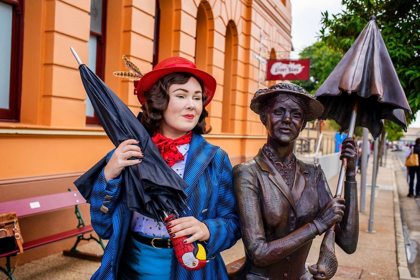 Young woman dressed as Mary Poppins beside a statue of the Mary Poppins character.