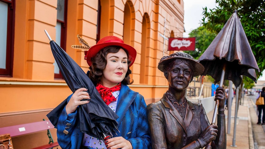 Young woman dressed as Mary Poppins beside a statue of the Mary Poppins character.