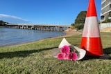 Pink flowers in a bouquet next to an orange traffic cone on a river bank.