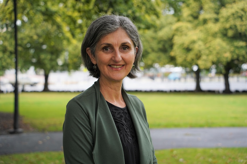 A woman stands in a park smiling at the camera.