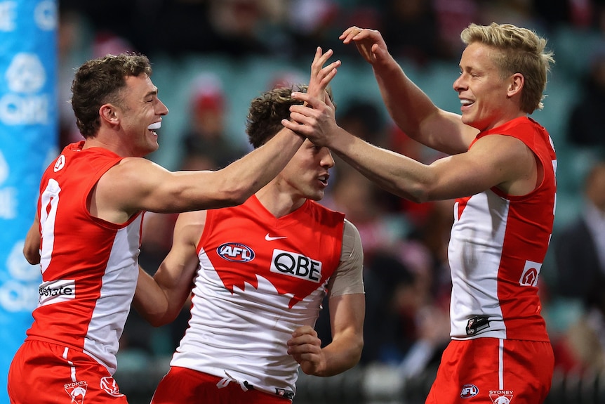 Tres jugadores de la AFL de los Sydney Swans se felicitan después de patear un gol.