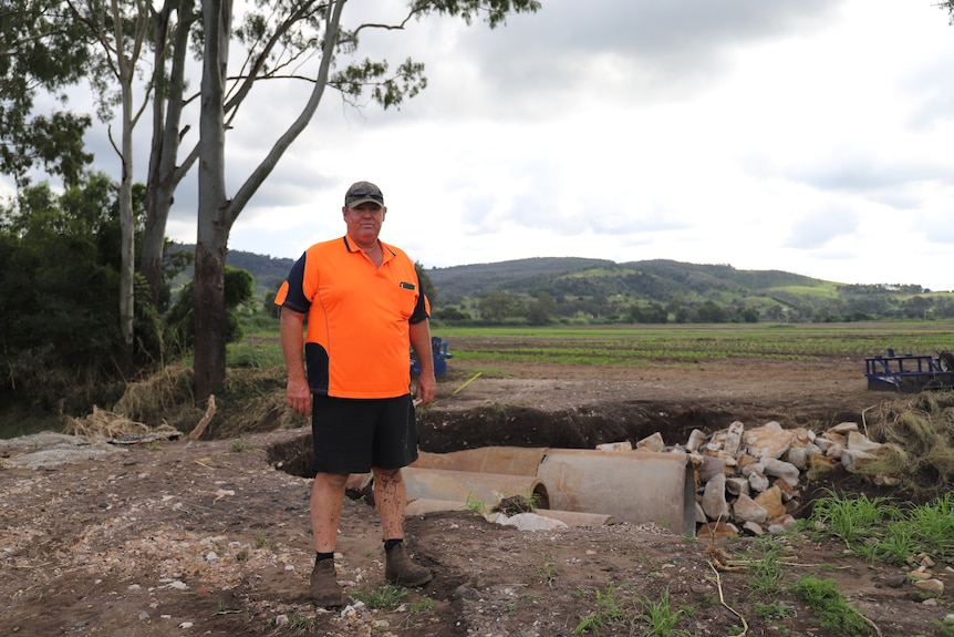 man in hi vis shirt standing in front of a flood damaged landscape