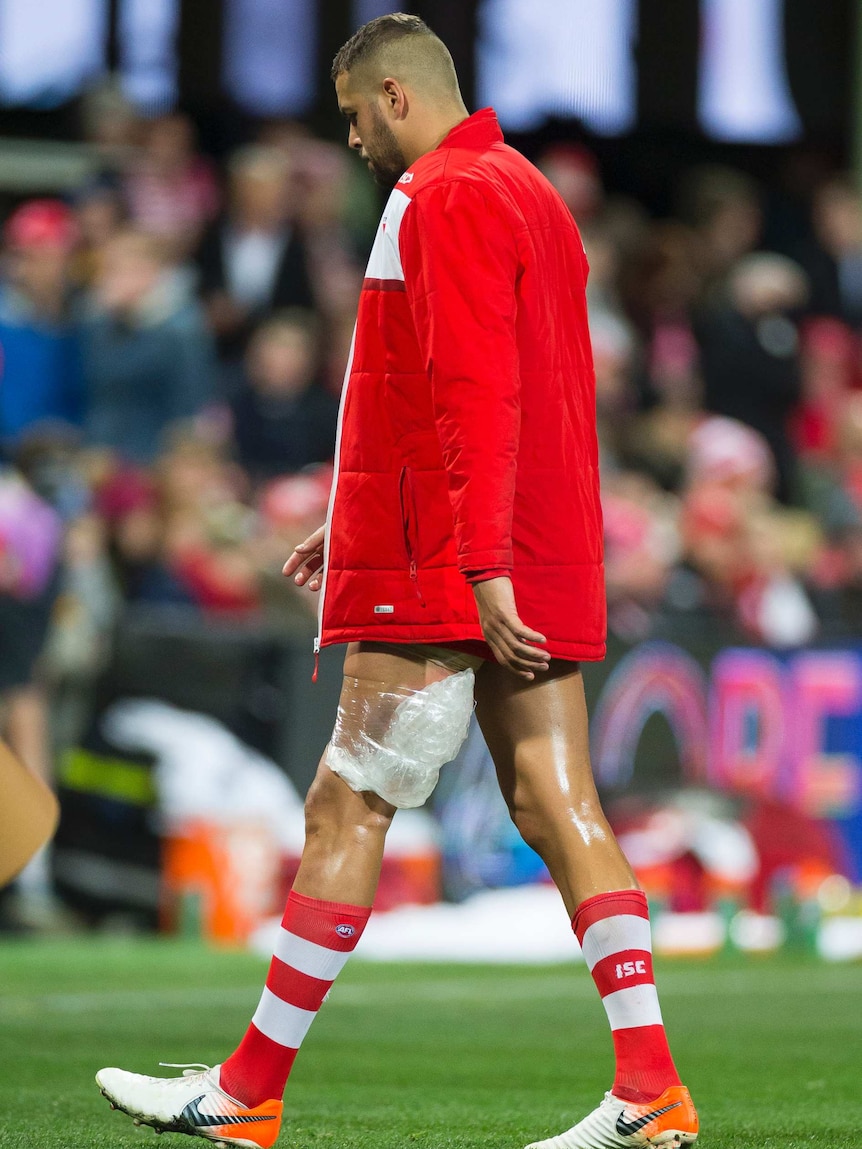 An AFL player walks off the field wearing a track suit top and with an ice pack applied to his left hamstring.