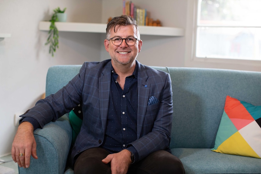 Man wearing suit, sitting on blue couch in living room.