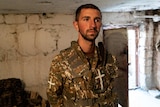A man in a rudimentary soldier's uniform looks contemplative in a unfinished room