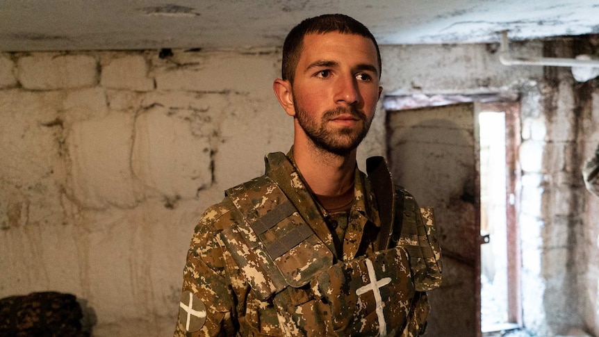 A man in a rudimentary soldier's uniform looks contemplative in a unfinished room