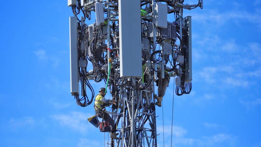 Two technicians work as they are harnessed at top of a mobile phone tower.