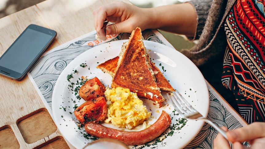 A person's breakfast plate with toast, scrambled eggs, roast tomato and sausage on it