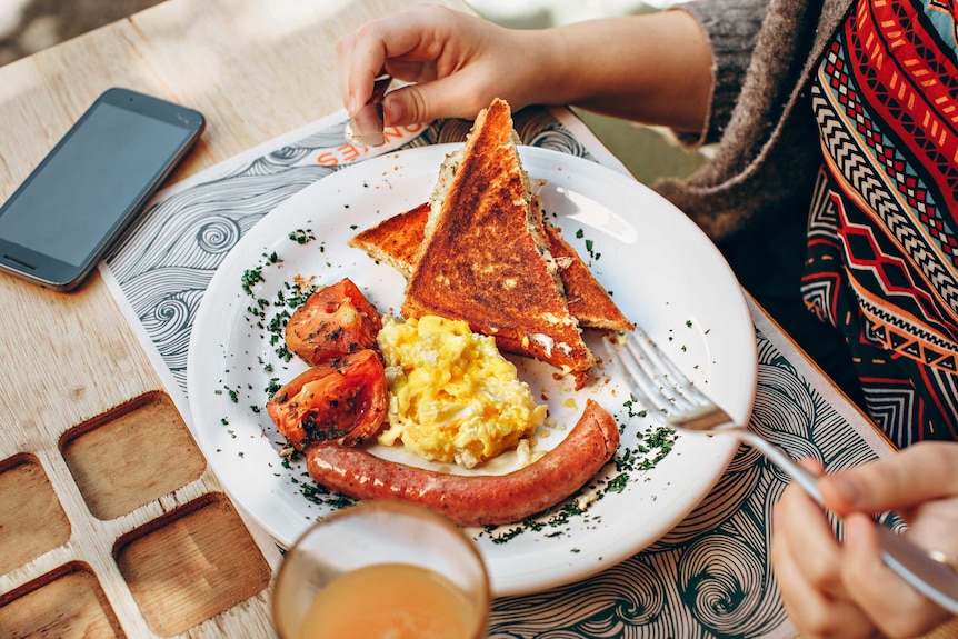 A person's breakfast plate with toast, scrambled eggs, roast tomato and sausage on it
