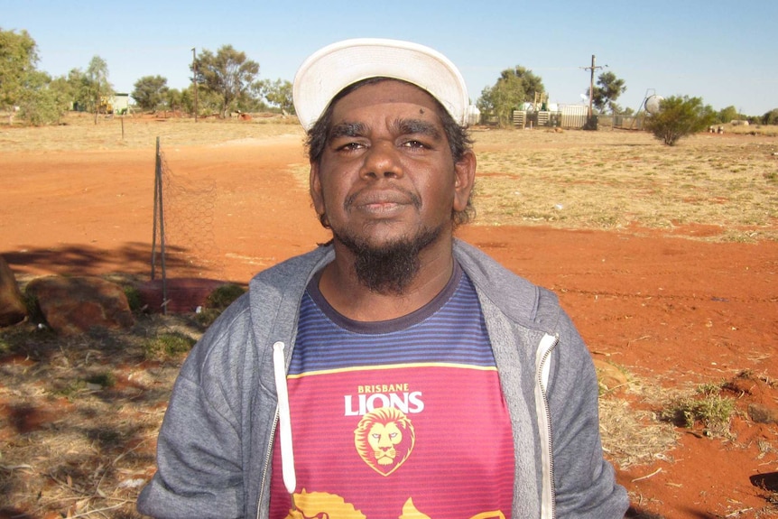 Gene Gibson stands with red earth, tin homes and powerlines in the background.