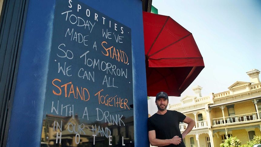 Launceston publican Nick Daking leans on a wall next to a sign outside Sporties pub.