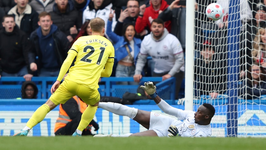 A Premier League footballer watches his shot loop over the prone goalkeeper into the net for a goal.