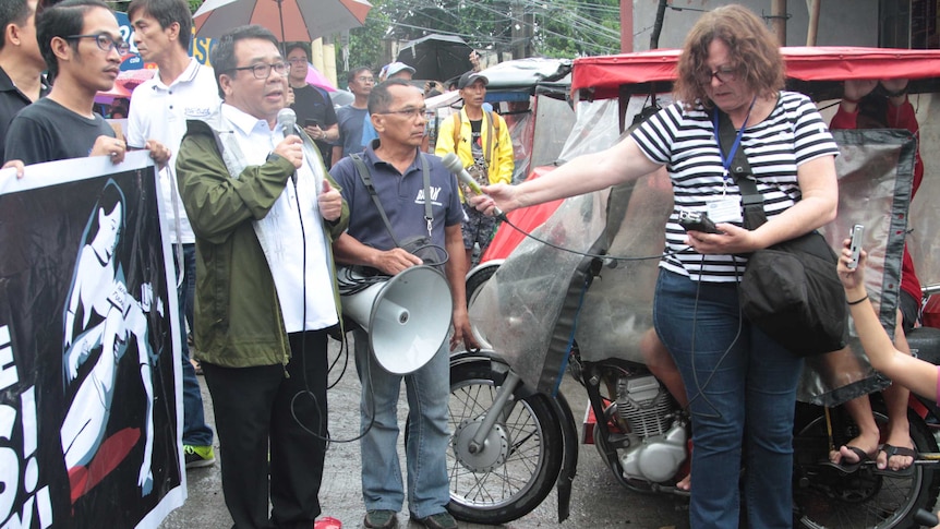 Ginny Stein holding microphone recording Neri Colmenare, chairman of opposition party Bayan Muna, speaking at a rally in Manila.