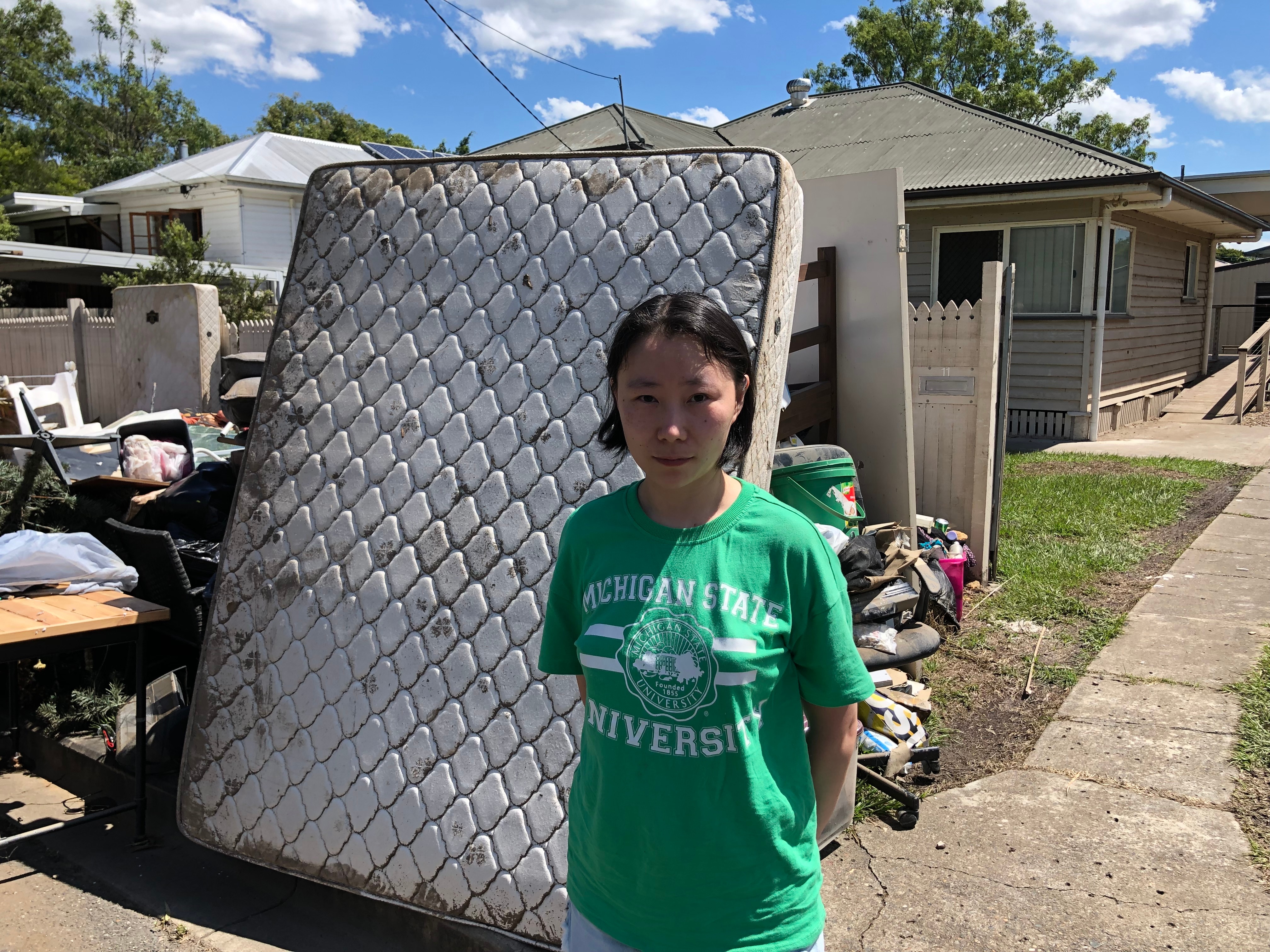 A woman standing in front of a ruined mattress outside her house