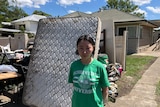 A woman standing in front of a ruined mattress outside her house