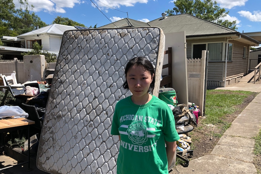 A woman standing in front of a ruined mattress outside her house