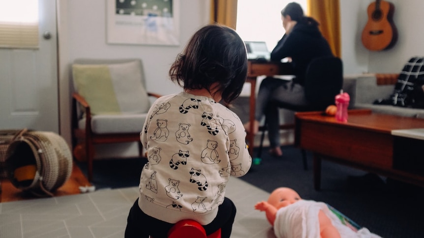 a woman working on her laptop as a child sits on the ground