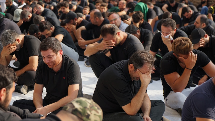 A group of men sitting on the floor weeps.