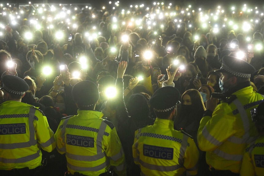 People gather and turn on their phone torches on police at a protest.