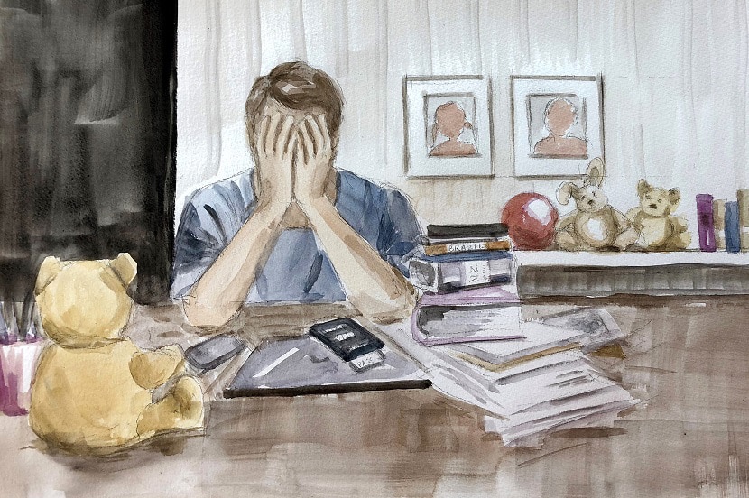 Dad holds head in hands sitting at a desk, surrounded by toys.