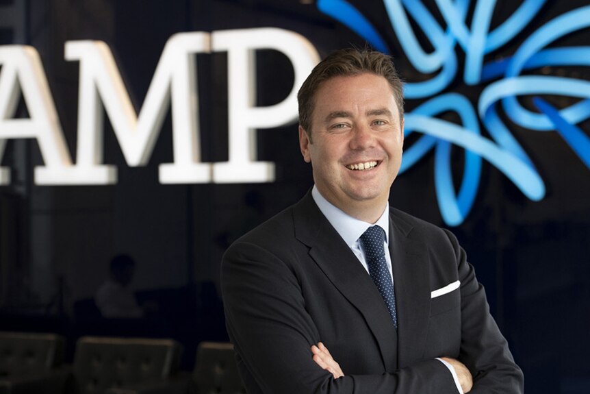 Alex Wade, a man in a suit, standing in front of the AMP logo.