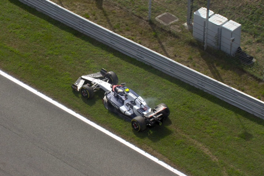 A blue and white F1 car on the side of the road in grass.