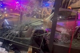 A silver car hits glass doors of restaurant, glass cracked and items damaged