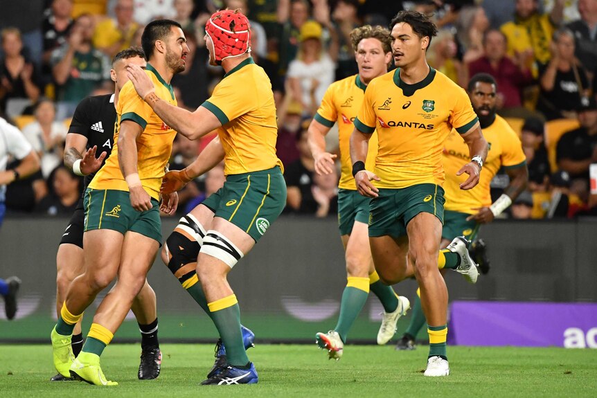 The Wallabies embrace one of their teammates after he scored a try against the All Blacks in Brisbane.