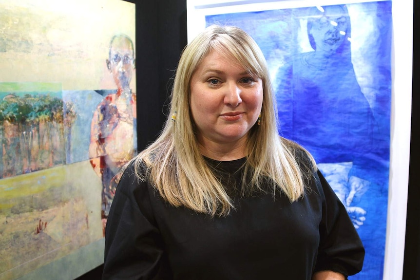 A Brisbane Portrait Prize judge standing in front of several paintings