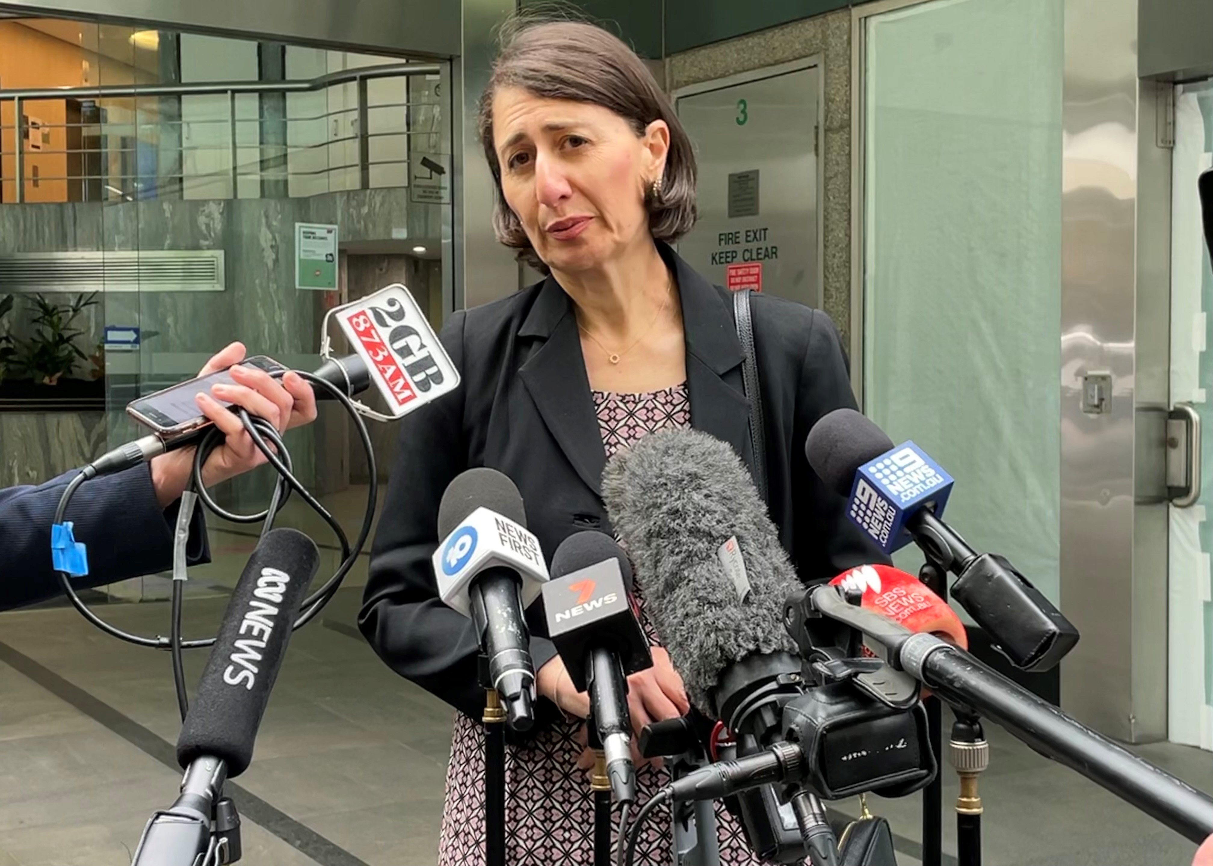 the former premier of new south wales gladys berejiklian stands outdoors behind microphones speaking to the media