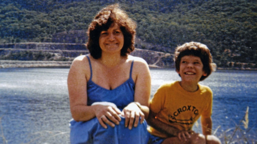 An old photograph of Maria James in a blue dress by the water with her young son Adam.