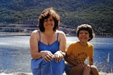 An old photograph of Maria James in a blue dress by the water with her young son Adam.