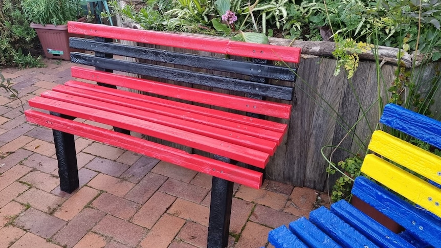 A red and black bench, which is made out of plastic.