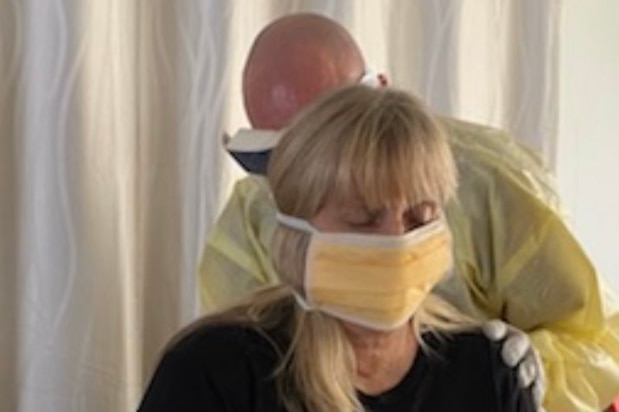 A man in yellow plastic examines a woman wearing a face mask while sitting down