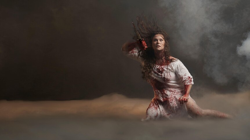 Australian soprano Jessica Pratt dressed in white, spattered with blood and clutching a dagger.