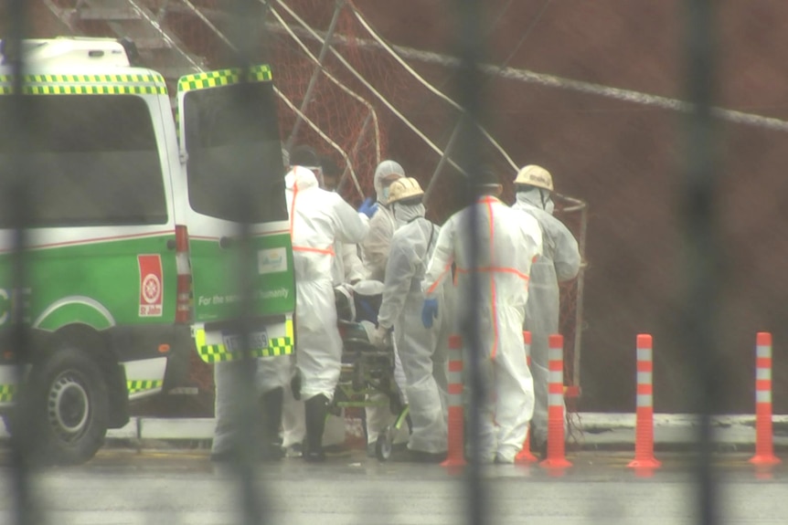 People in hazmat suits on a dock in front of a bulk carrier.