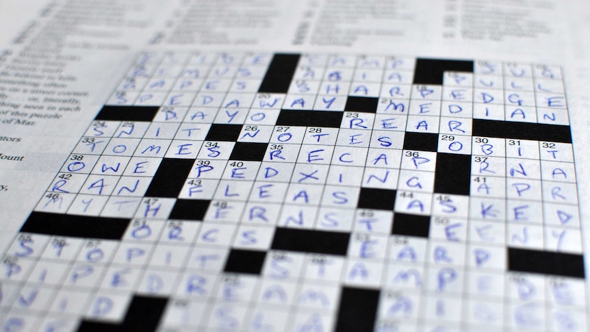 A close-up of a completed crossword puzzle, that has its answers marked in capital letters in blue pen.