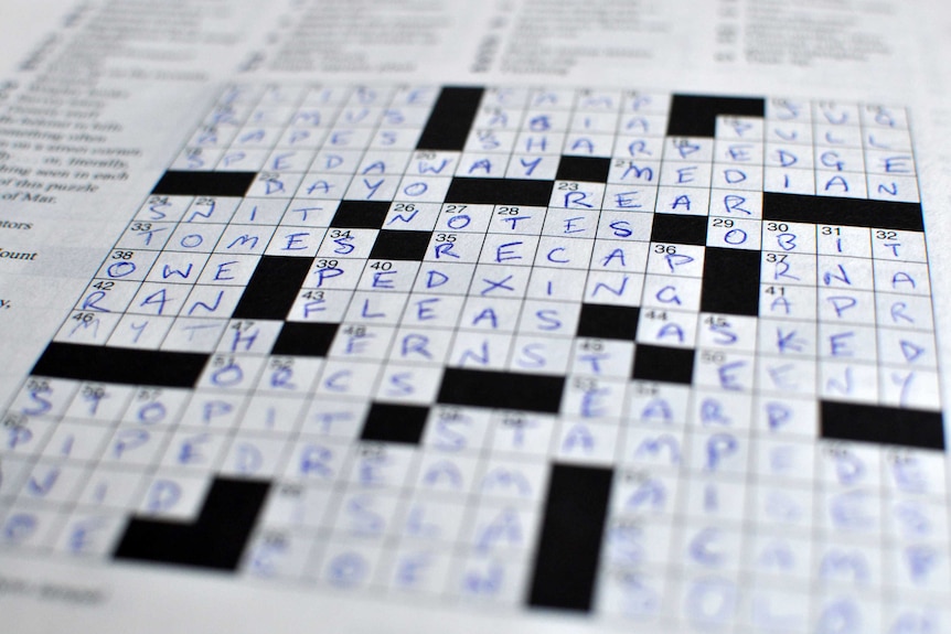 A close-up of a completed crossword puzzle, that has its answers marked in capital letters in blue pen.