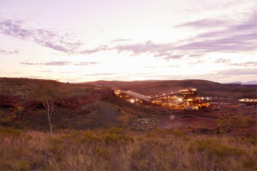 A mining operation at dusk in the Pilbara among a red rocky range and spinifex.