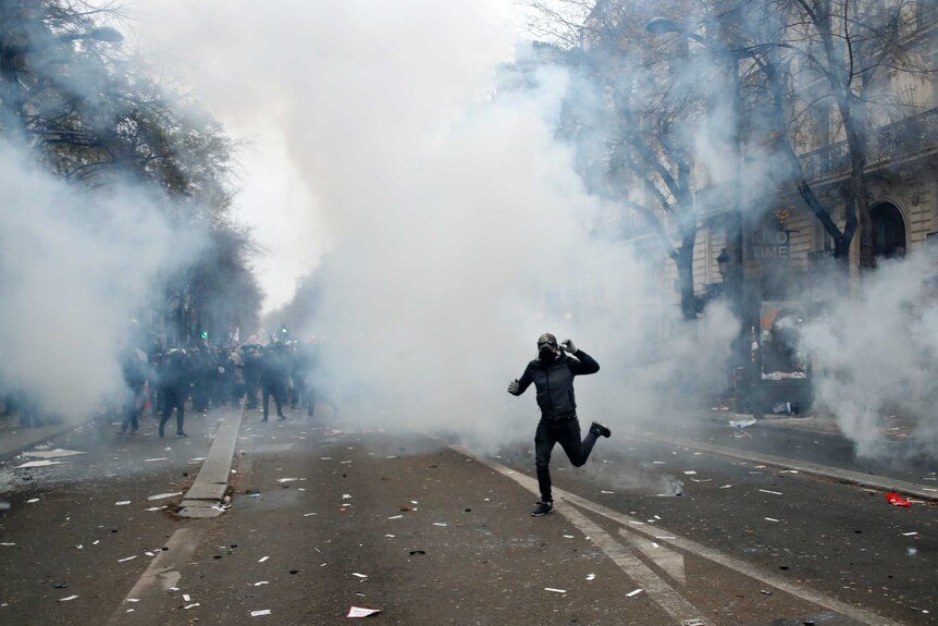 A youth runs through a cloud of tear gas covering his face.