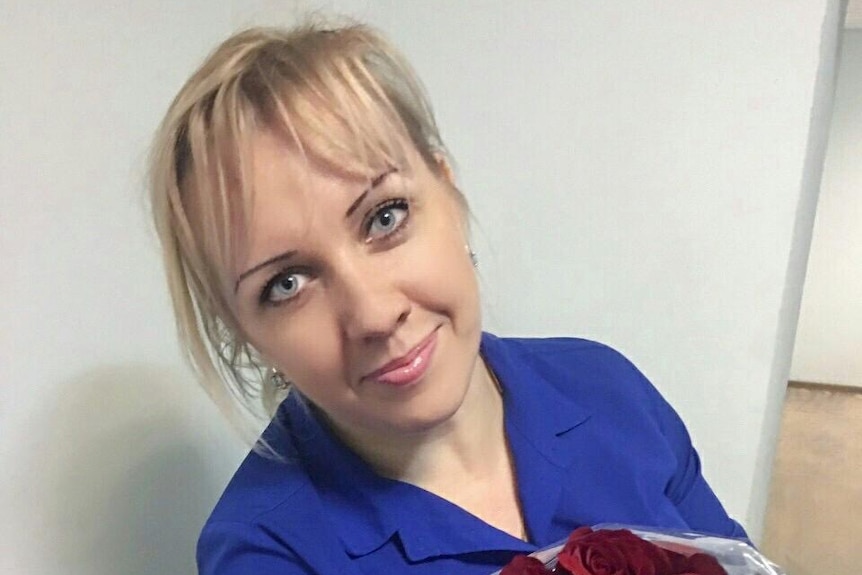 A blonde woman smiling with a bouquet of roses.