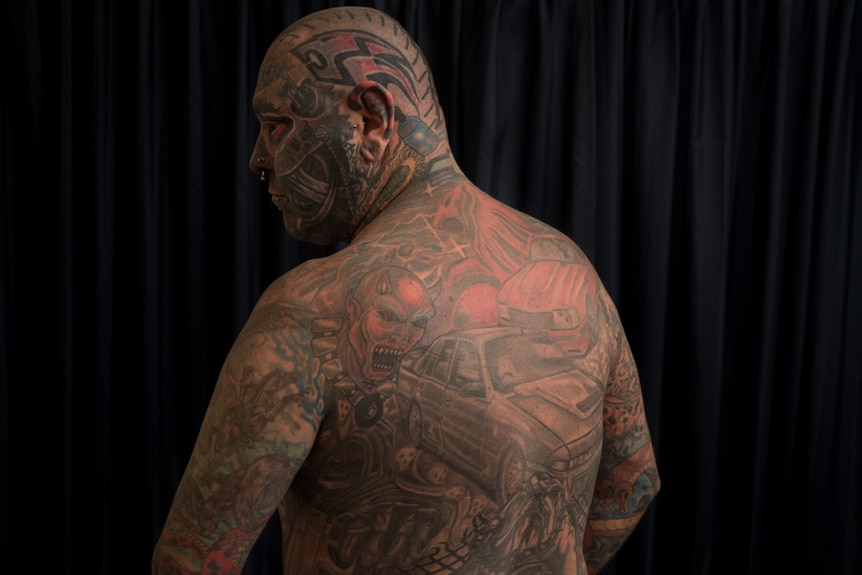 Tattboy's back art work includes two cars and a bulldog.