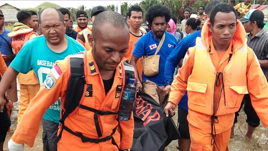 Dozens of locals and rescue workers walk through flood-affected areas, carrying a body inside a body bag