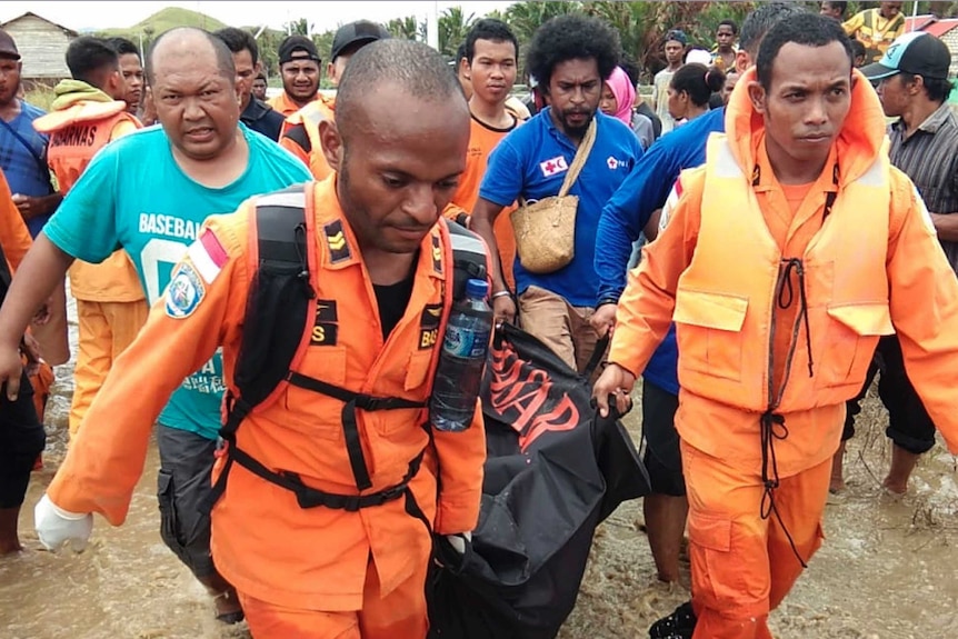 Dozens of locals and rescue workers walk through flood-affected areas, carrying a body inside a body bag