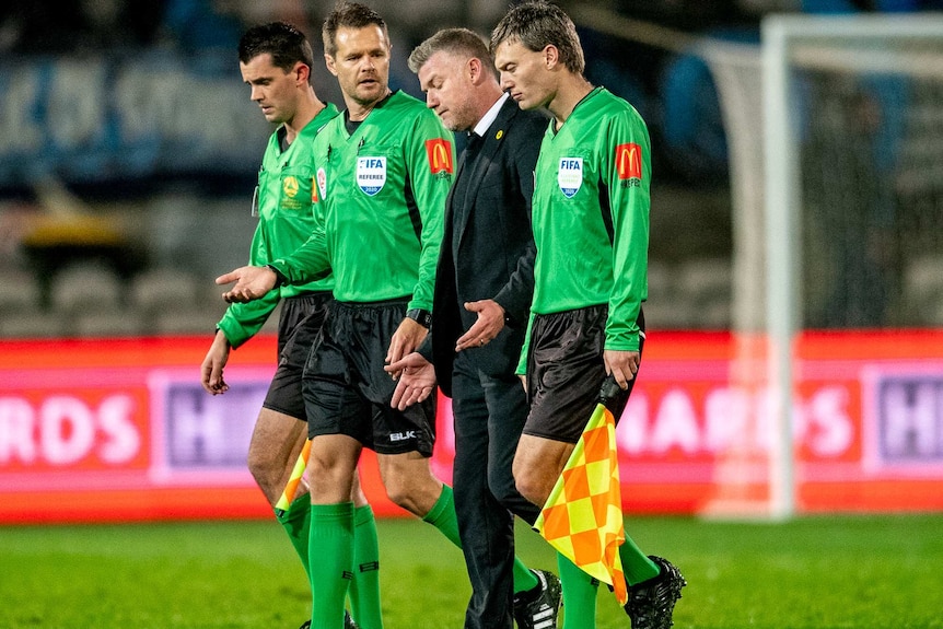 Ufuk Talay walks next to three men wearing green shirts