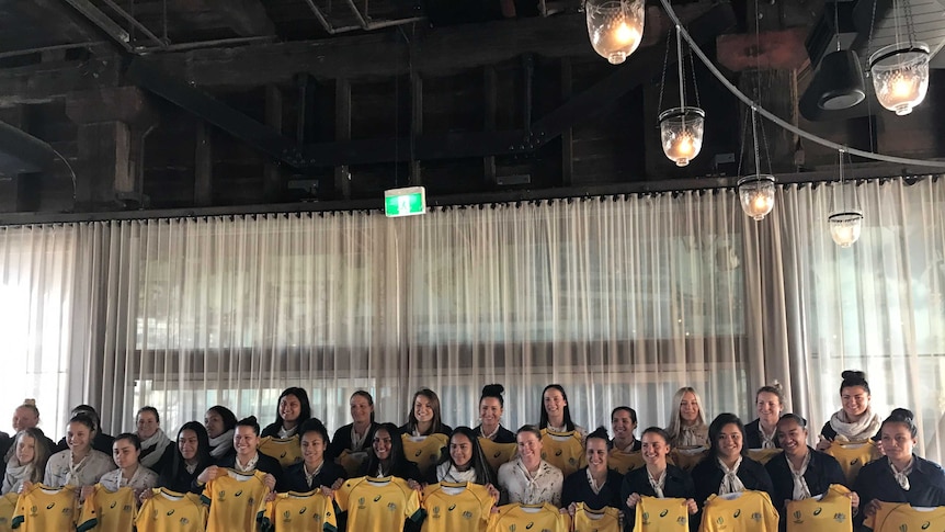 A group of 28 women with gold rugby union jerseys at a presentation in Sydney.