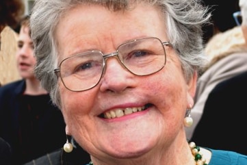A close up image of a smiling woman with grey hair and glasses